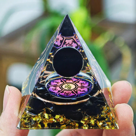 Pyramid-shaped crystal with colorful interior design held by a hand against a blurred natural background