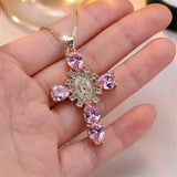 Gold necklace with pink gemstone pendant held in a hand against a blurred background