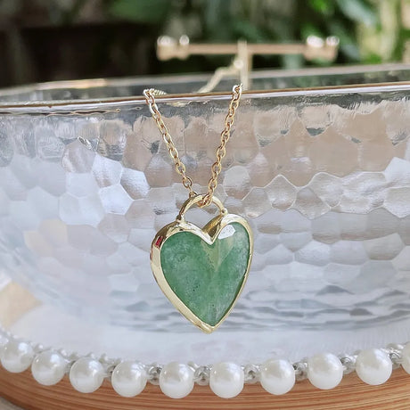 Gold necklace with a green heart pendant on a marble surface