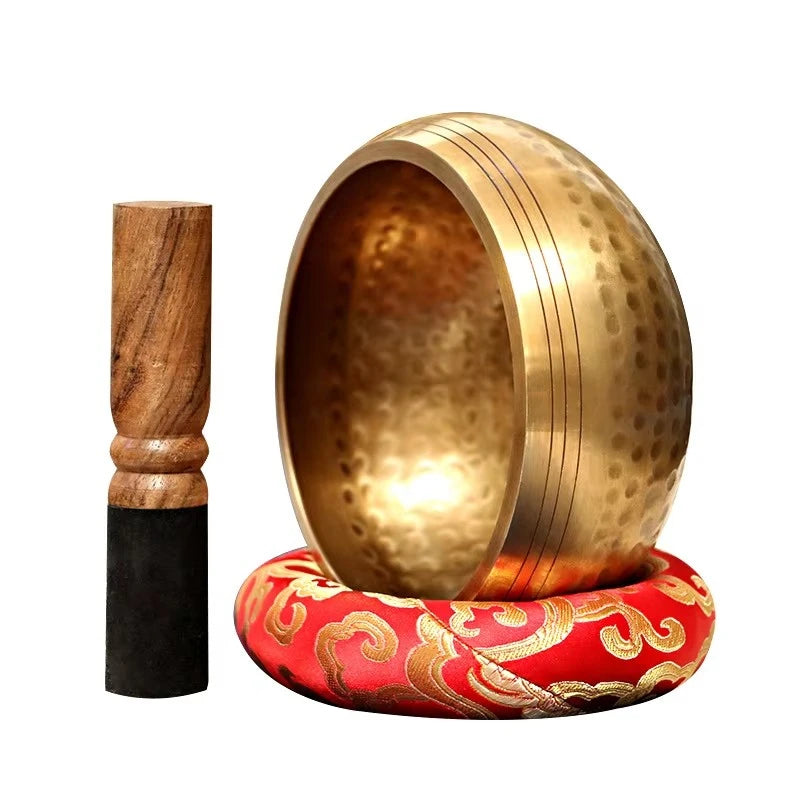 Gold singing bowl with wooden striker and red cushion on a white background