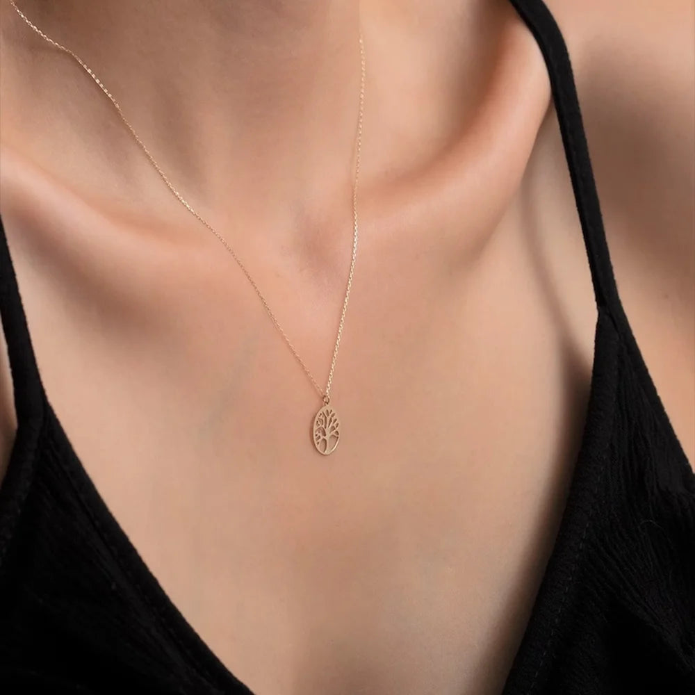 Gold necklace with a tree pendant on a person wearing a black top.