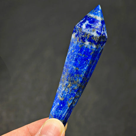 Blue crystal held by a hand against a dark background