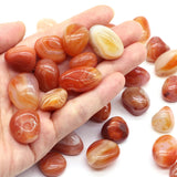 Hand holding a collection of orange and white marbled stones on a white background