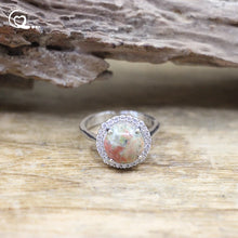 Silver ring with a large gemstone and smaller stones on a wooden surface
