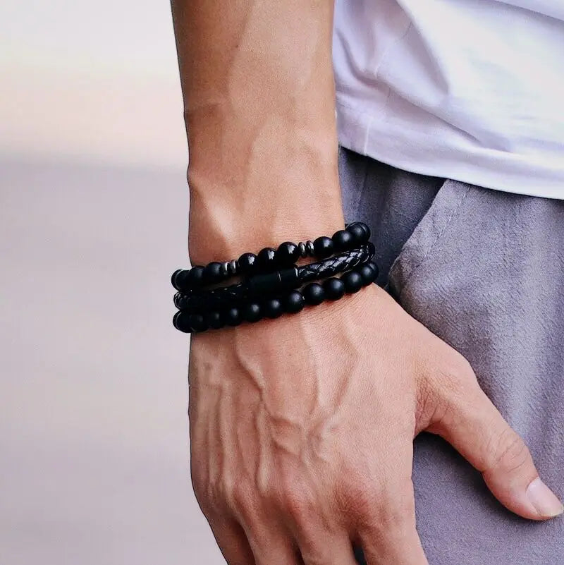 Close-up of a wrist wearing multiple black bracelets on a neutral background