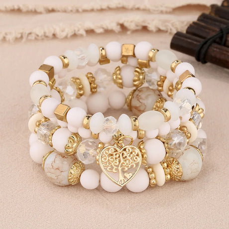 Stack of white and gold beaded bracelets with a heart charm on a beige fabric background