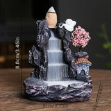 Decorative fountain with rocks, water, and a small house on a wooden surface.