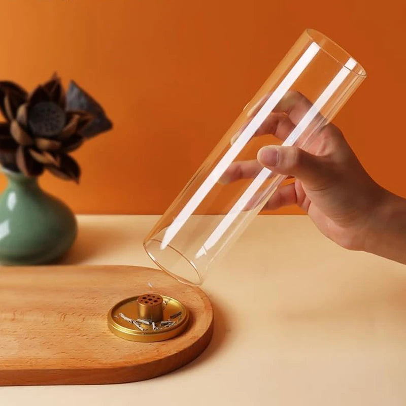 Hand holding a clear glass tube over a wooden base with a small object inside, against an orange wall.