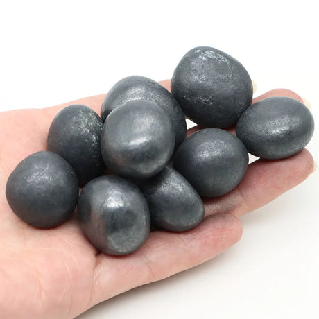 Hand holding a handful of dark gray stones against a white background