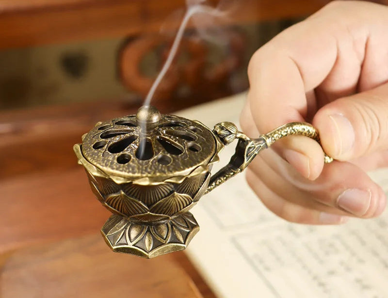 Hand holding a traditional incense burner with smoke rising, on a wooden surface.