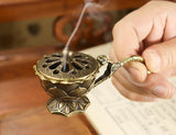 Hand holding a traditional incense burner with smoke rising, on a wooden surface.