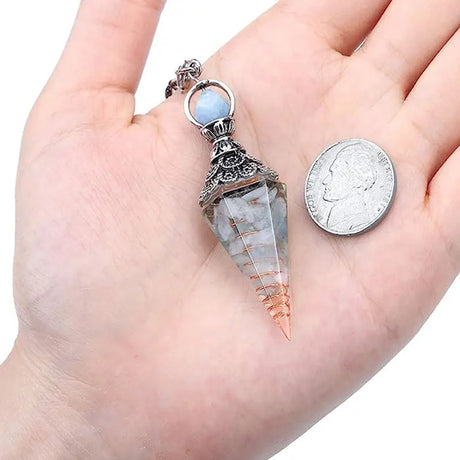 Crystal pendant held in a hand with a coin for scale on a white background