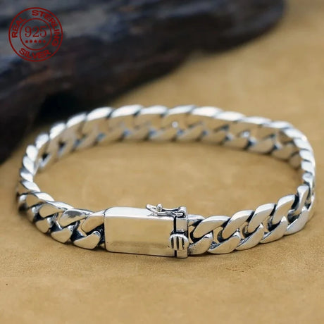 Silver chain bracelet on a beige surface with a brand logo in the corner.