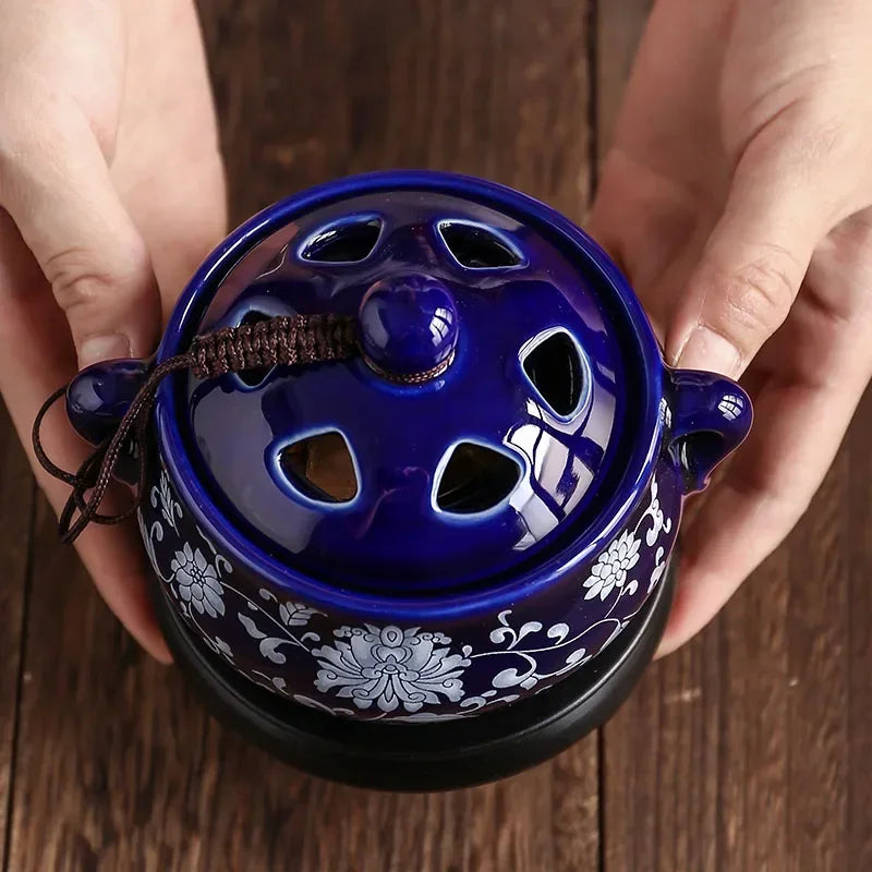 Blue ceramic incense burner with floral patterns held by hands on a wooden surface