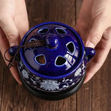 Blue ceramic incense burner with floral patterns held by hands on a wooden surface