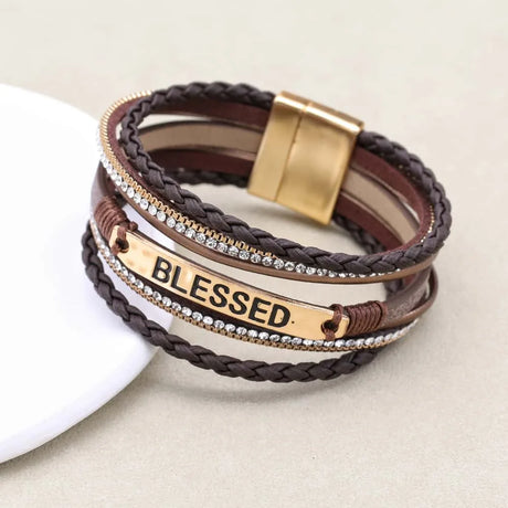 Multistrand leather bracelet with gold accents and 'BLESSED' tag on a beige background