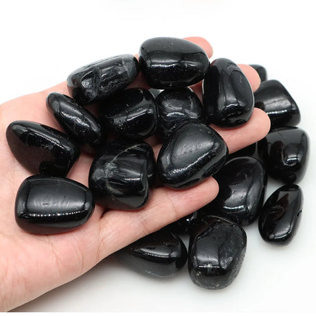 Hand holding a collection of black stones on a white background