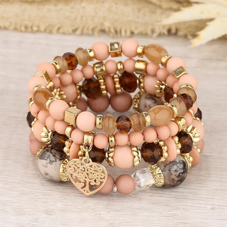 Stack of beaded bracelets with gold accents and a heart charm on a neutral background