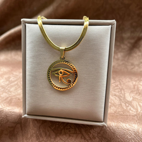 Gold necklace with an eye pendant on a white box against a brown background