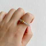 Hand wearing a ring with gold and clear beads on a plain background