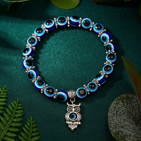Bracelet with blue and black beads and an owl charm on a green leafy background
