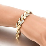 Gold bracelet with leaf design on a wrist against a neutral background
