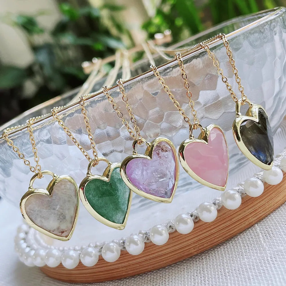 Heart-shaped pendants on gold chains displayed on a decorative stand with a blurred greenery background.