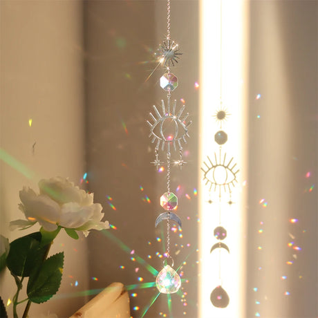 Decorative hanging crystal with sun, moon, and eye designs in front of a window with sunlight filtering through.