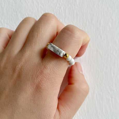 Hand wearing a ring with marble and gold design on a plain background