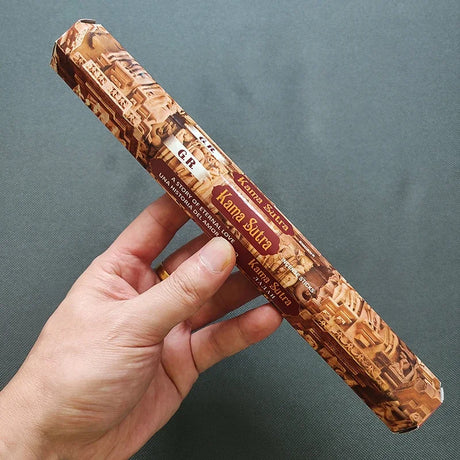 Hand holding a decorative book titled 'Kama Sutra' against a gray background
