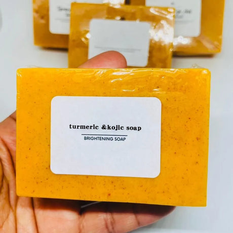 Yellow bar of turmeric & kojic soap held by a hand with a white label.