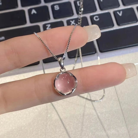 Silver necklace with a pink pendant held by a hand in front of a laptop keyboard.