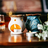 Two ceramic wax warmers with candles on a wooden surface.