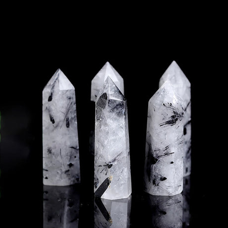 Three crystal points with black inclusions on a reflective surface against a black background