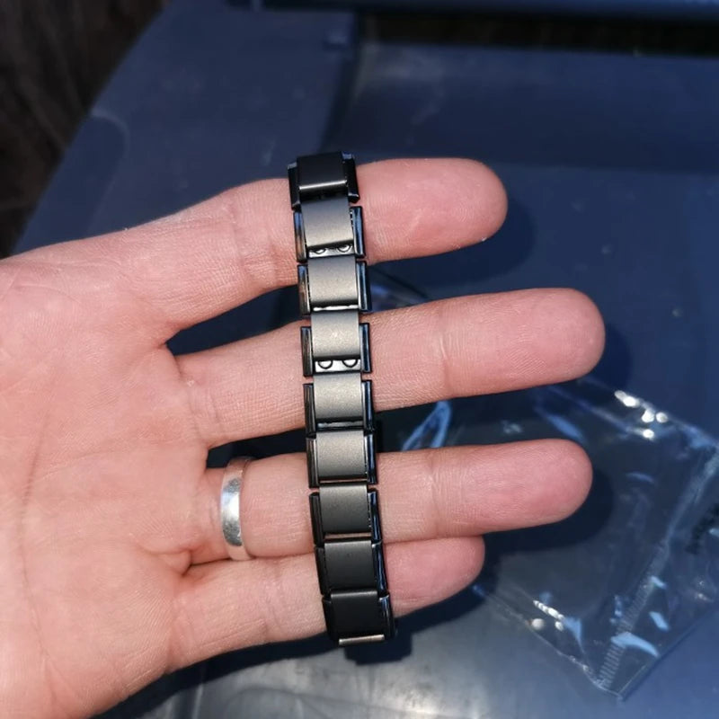 Hand holding a black and silver metal bracelet against a blue background