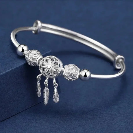 Silver bracelet with decorative beads and feathers on a blue background
