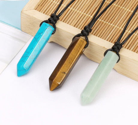 Three crystal necklaces in blue, brown, and green on a bamboo mat with a light blue card in the background.
