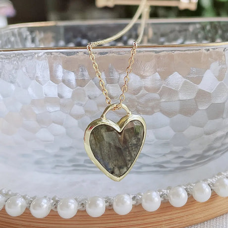 Gold heart-shaped necklace with a stone pendant on a marble surface