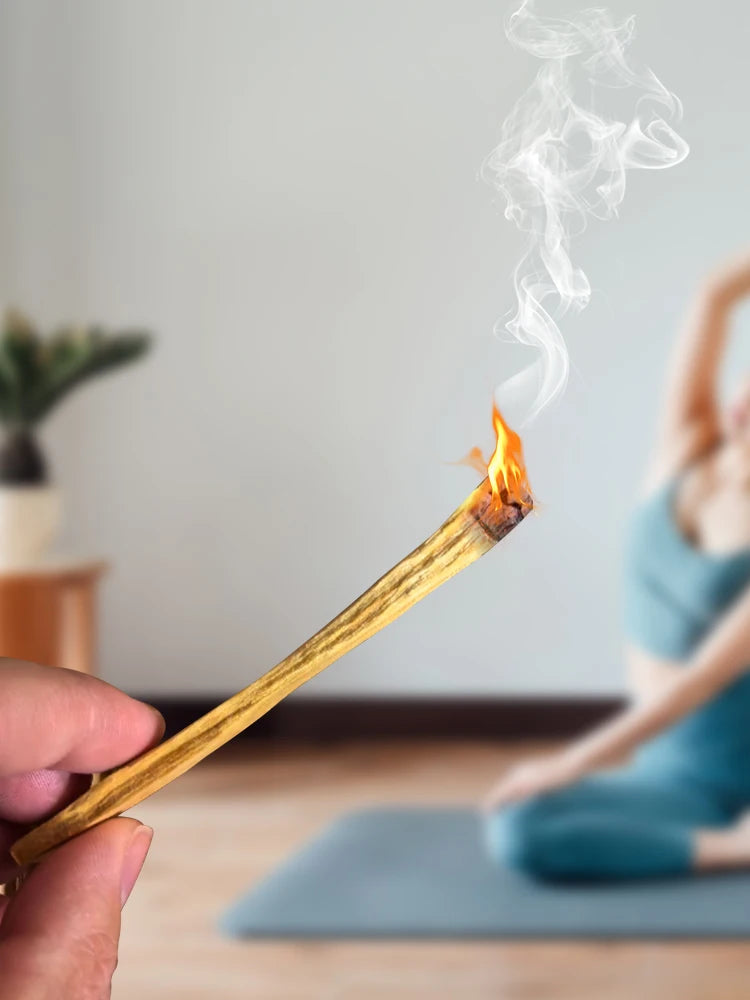Person holding a lit match with smoke, blurred background of a person sitting on a yoga mat.