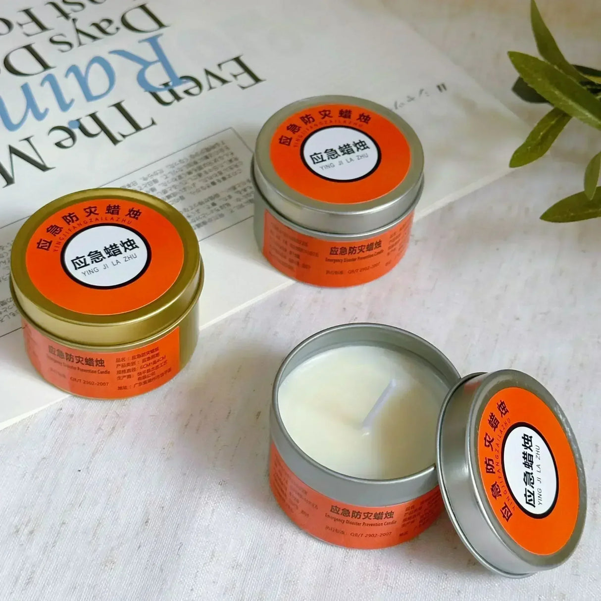 Three tins of candles with orange labels on a newspaper background