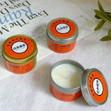 Three tins of candles with orange labels on a newspaper background