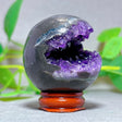 Geode crystal with purple interior on a wooden stand against a green leafy background