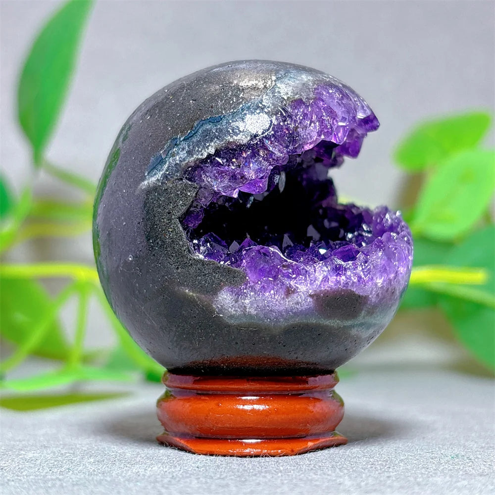 Geode crystal with purple interior on a wooden stand against a green leafy background