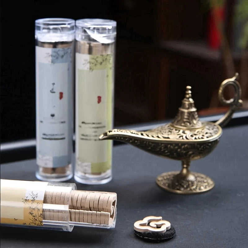Two cylindrical containers with a gold genie lamp and small round object on a dark surface.