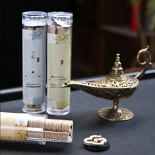 Two cylindrical containers with a gold genie lamp and small round object on a dark surface.