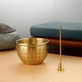 Gold incense bowl and stick on a wooden surface with a blurred background