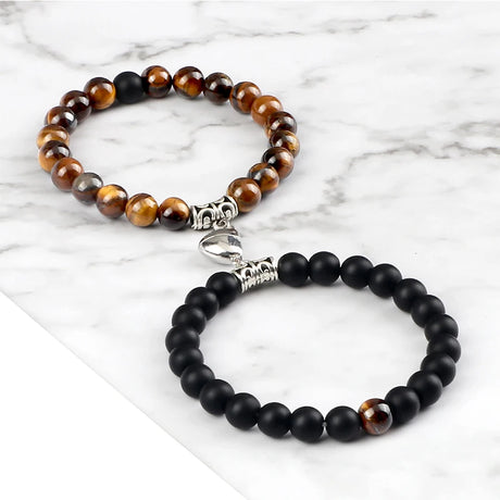 Two beaded bracelets, one with brown and black beads and the other with black beads, on a marble surface.