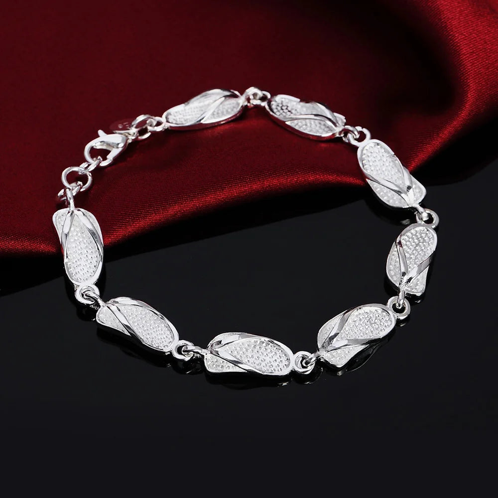 Silver bracelet with leaf-like links on a dark surface with red fabric background