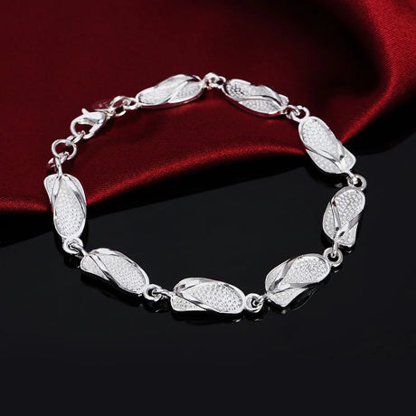 Silver bracelet with leaf-like links on a dark surface with red fabric background