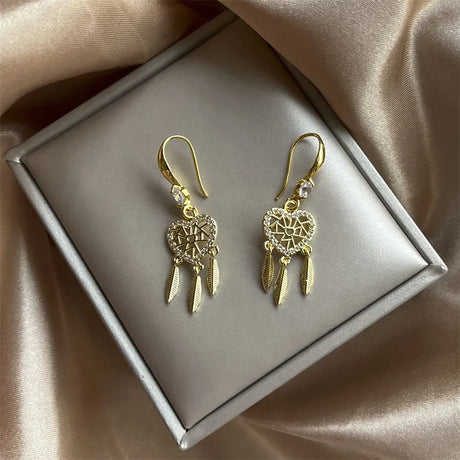 Gold earrings with intricate designs on a gray box with beige fabric background